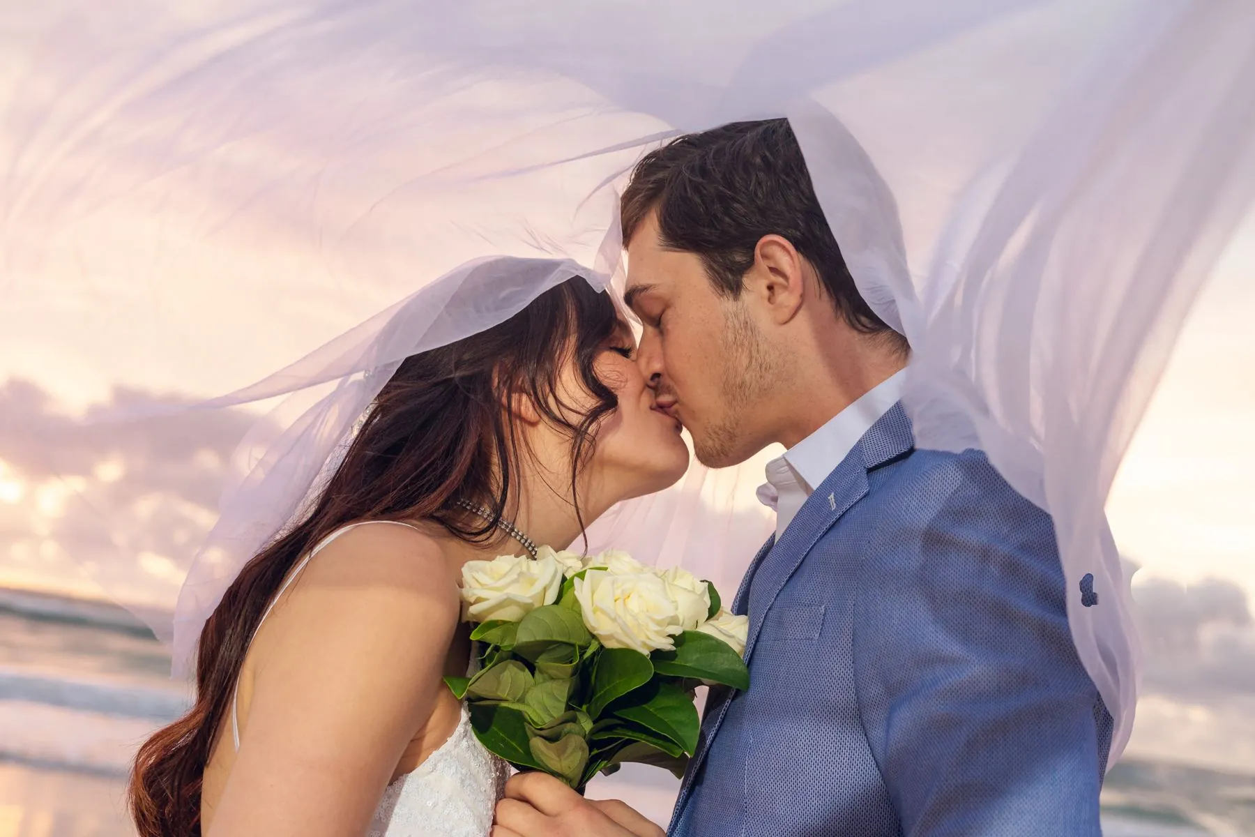 Beach wedding veil kiss at sunset