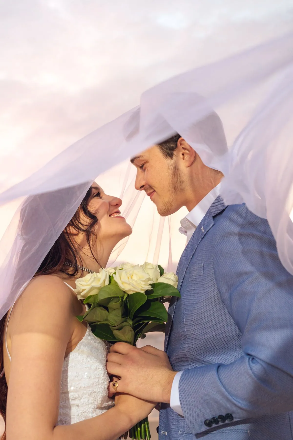 Bride under her veil at a beach wedding, golden hour